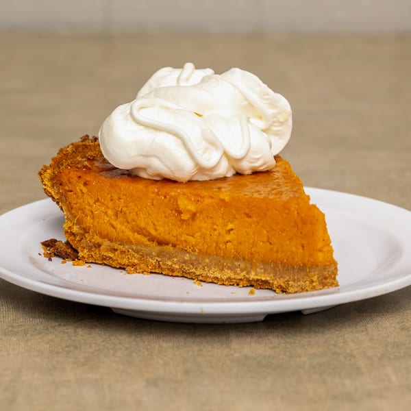 A slice of IDA MAE’S sweet potato pie with a dollop of whipped cream on a white plate.