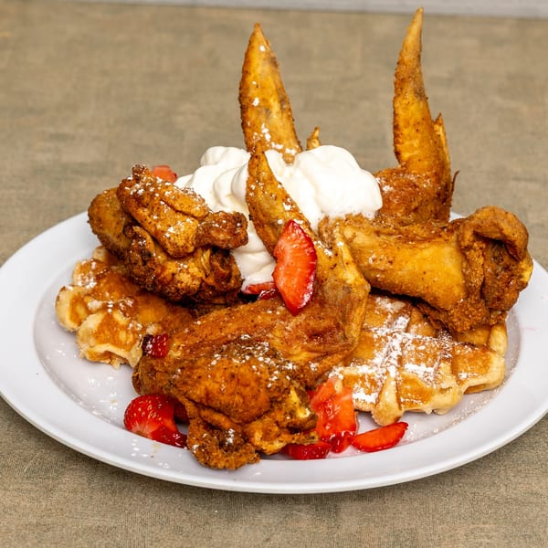 IDA MAE’S chicken and waffles with whipped cream, strawberries, and powdered sugar.